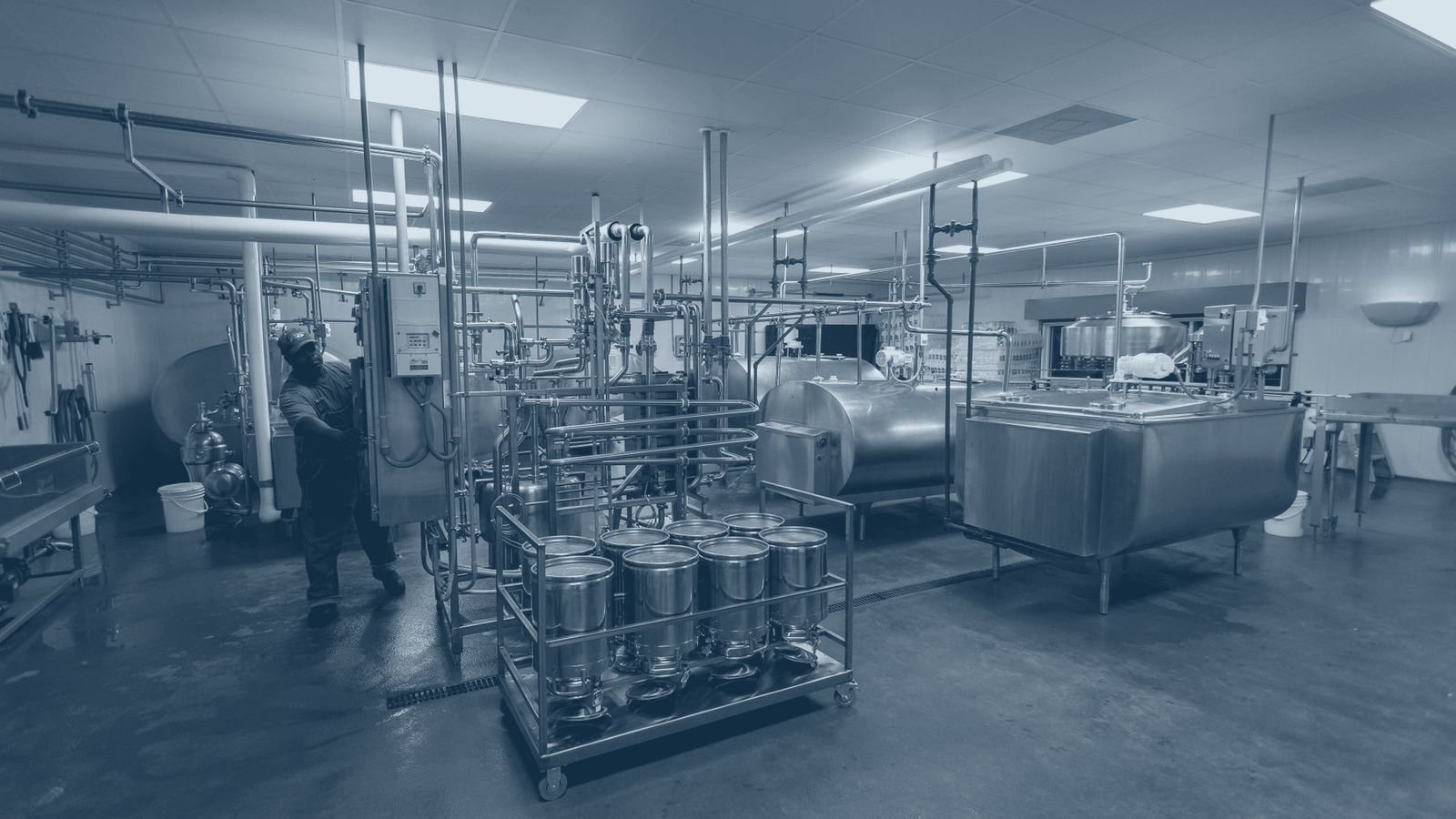 Stainless steel process tanks and pipework inside a working dairy processing hall